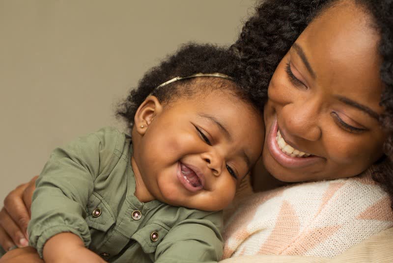 Mãe sorrindo com o bebê encostado no rosto, os dois rindo juntos em um momento de carinho